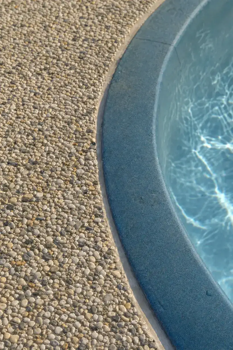 Close detail of an exposed aggregate concrete pool surround edge meeting blue swimming pool coping at a Cottesloe coastal home