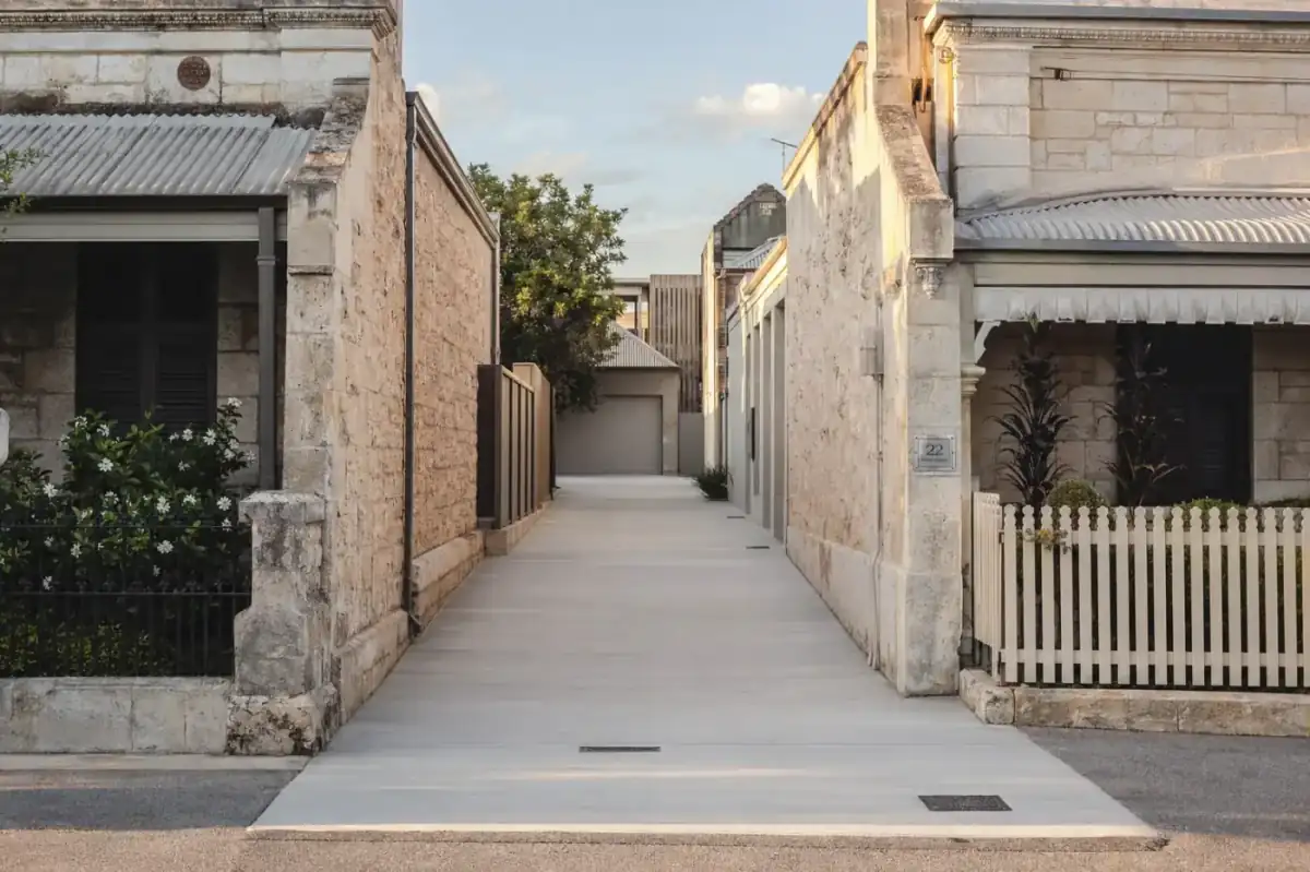 Newly poured concrete driveway between two heritage limestone cottages in central Fremantle, weathered limestone walls, port-suburb late afternoon light