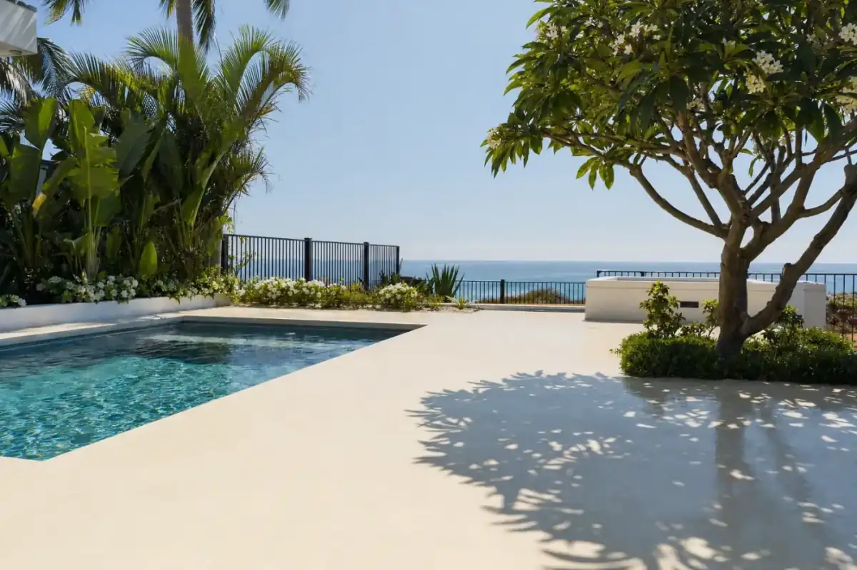 Newly poured liquid limestone pool surround beside a residential swimming pool in Scarborough, cream pale concrete reflecting bright sunlight, ocean visible in distance