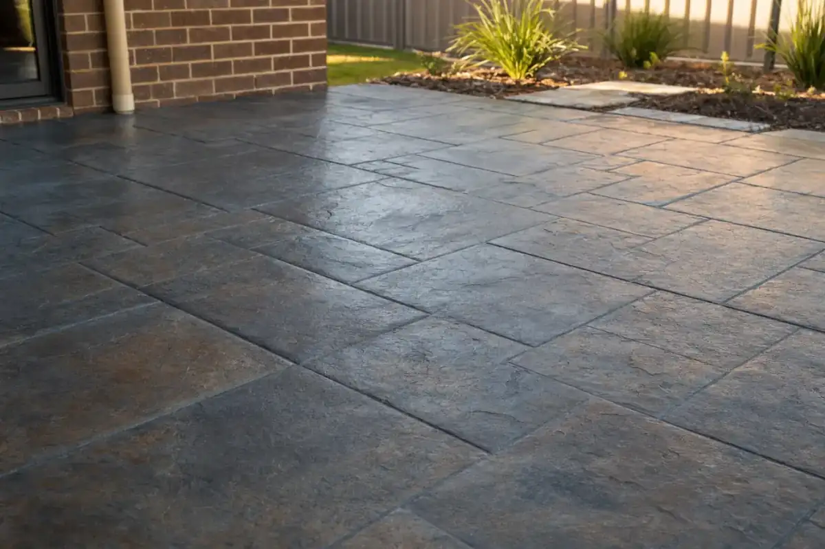 Slate-pattern stamped concrete patio in a Perth backyard, charcoal grey with subtle rust tones in late afternoon raking light